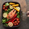 A piece of fish lying next to some vegetables. They are ready to be grilled.