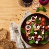 A plate of salad lying next to a glass of red wine.